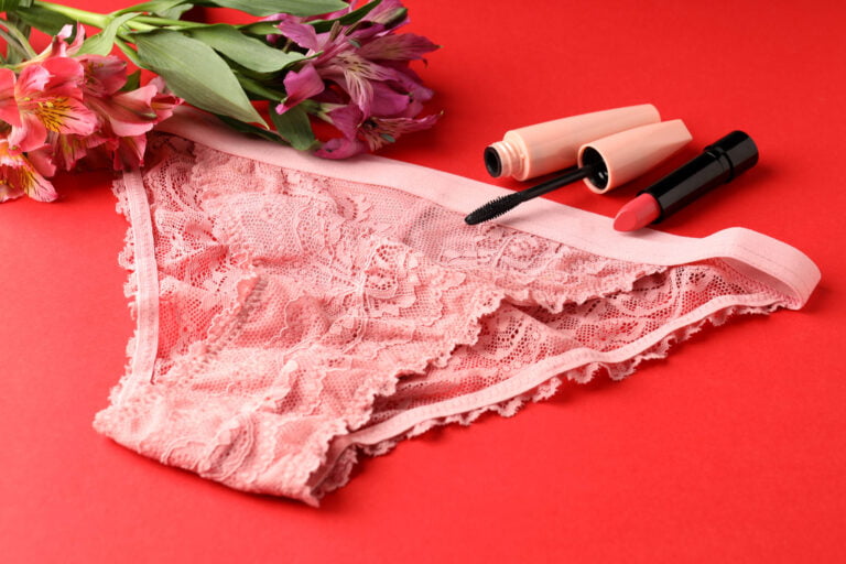 Pink lace women's underwear, lipstick, and mascara on red background
