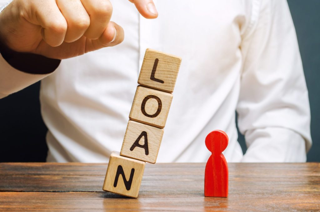 Wooden blocks with the word Loan fall on a miniature person